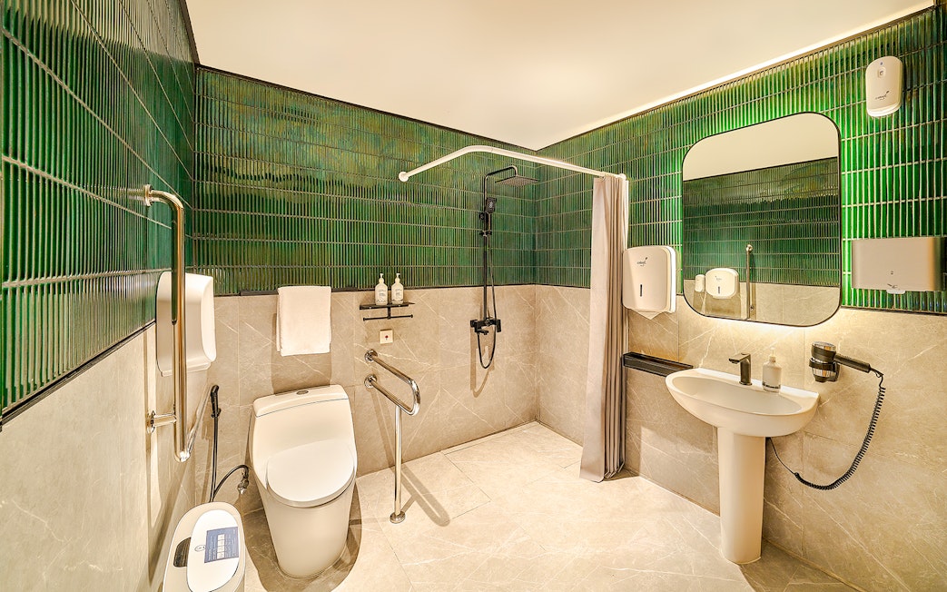 Accessible premium restroom with green tiles, shower, and modern amenities for lounge users.