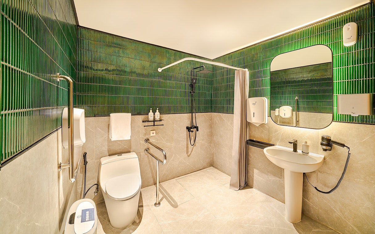 Accessible premium restroom with green tiles, shower, and modern amenities for lounge users.