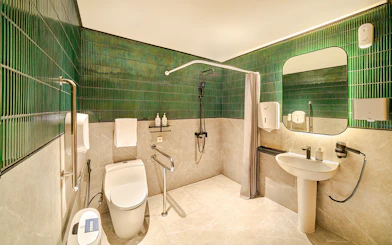 Accessible premium restroom with green tiles, shower, and modern amenities for lounge users.