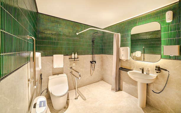 Accessible premium restroom with green tiles, shower, and modern amenities for lounge users.