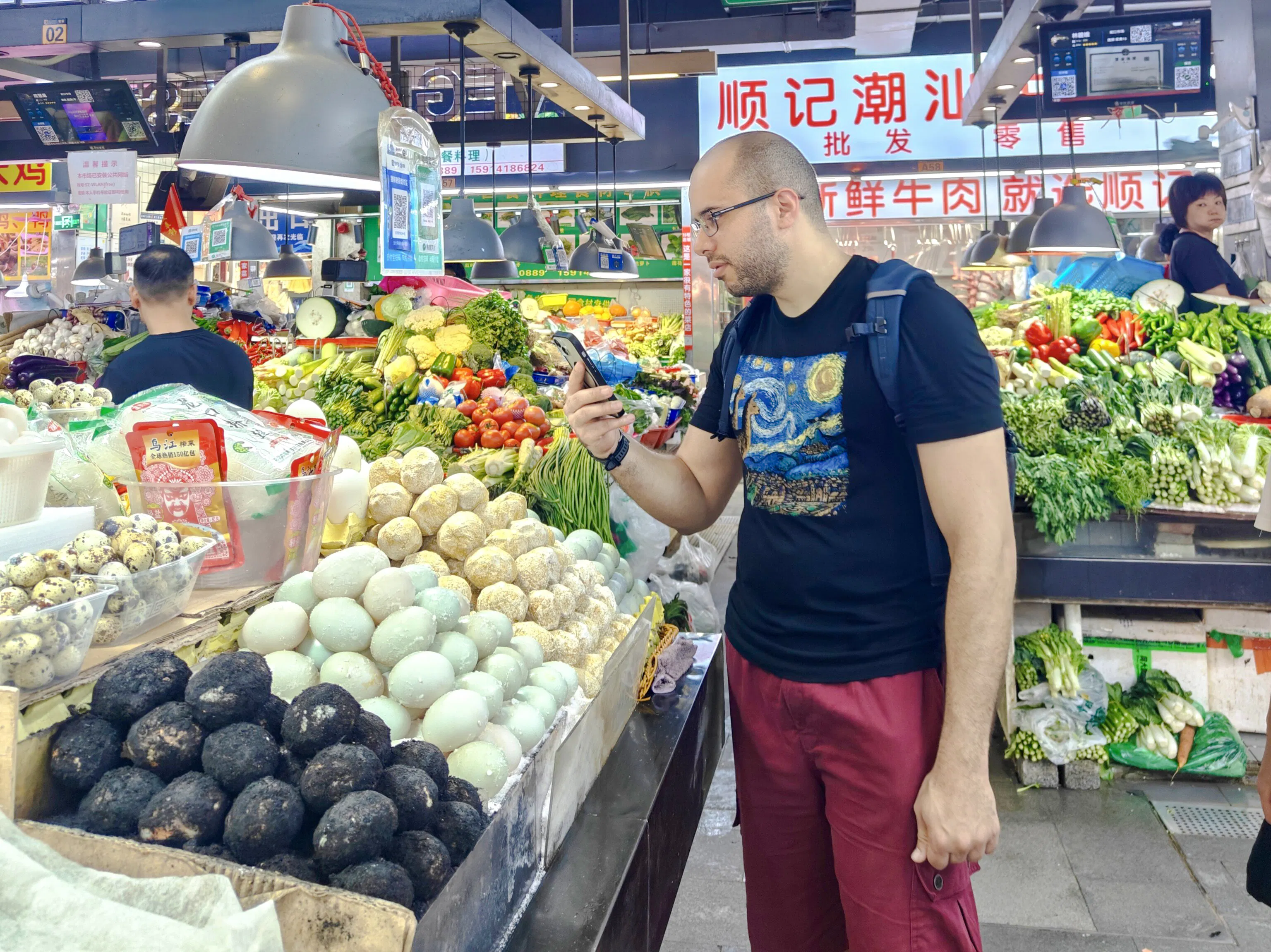 Man exploring Shenzhen market, surrounded by fresh vegetables and eggs, using a smartphone.