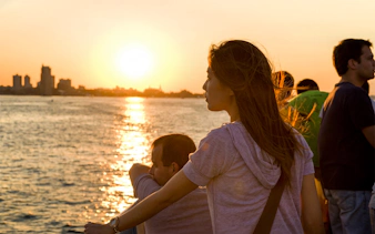 People enjoying a sunset cruise on the water with Boston skyline in the background.