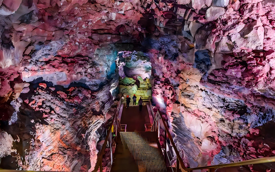Guests walking on a metal bridge inside Raufarhólshellir Lava Cave, Iceland.