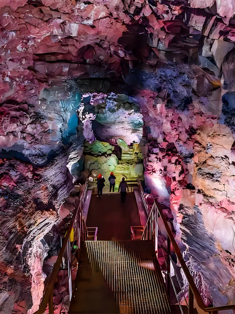 Guests walking on a metal bridge inside Raufarhólshellir Lava Cave, Iceland.