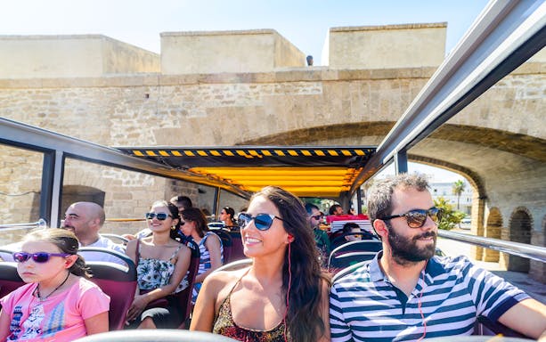 Passengers enjoying a Hop-On Hop-Off bus tour in Cadiz, passing under a historic stone arch.