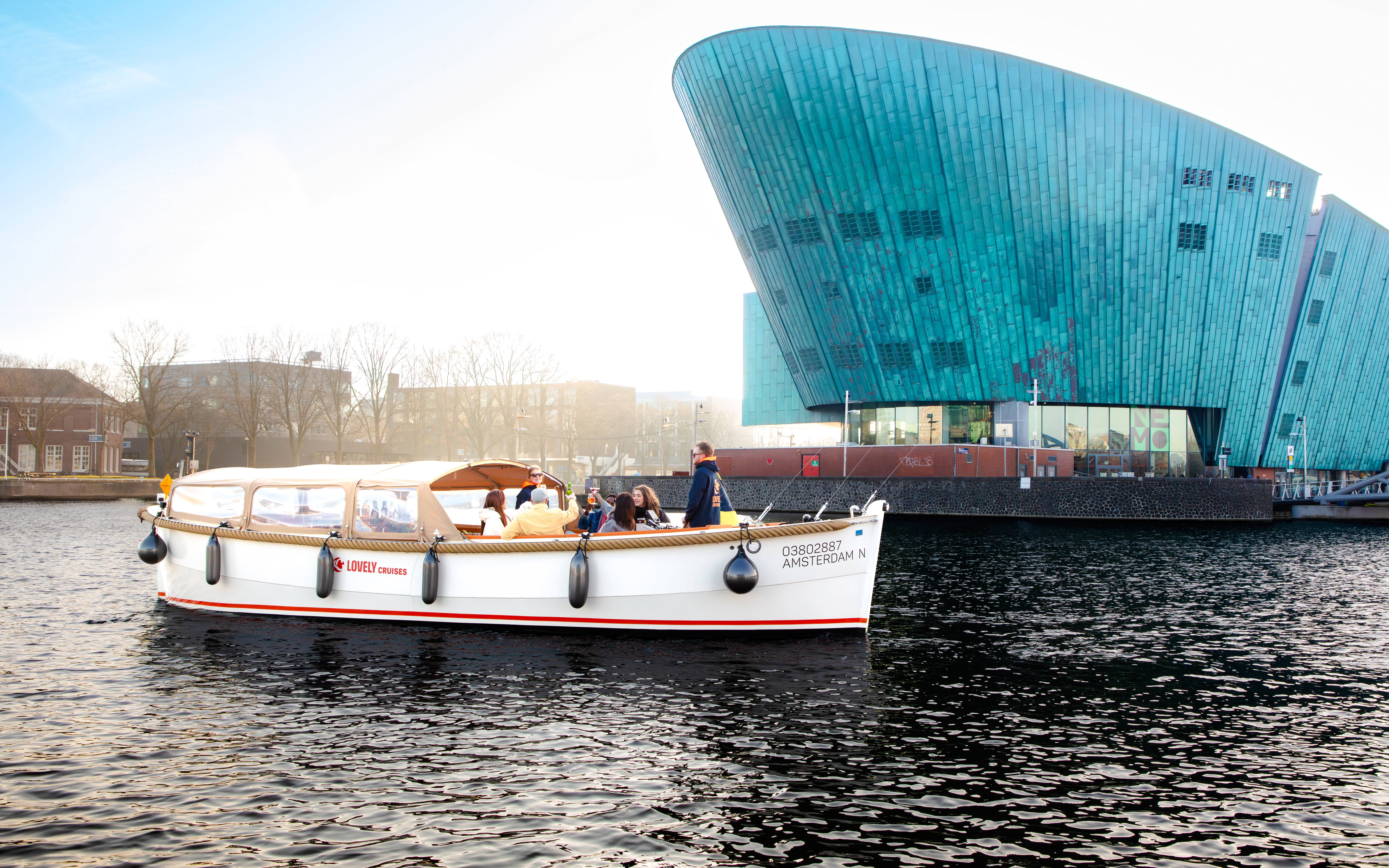 Open boat cruise near NEMO Museum in Amsterdam with passengers enjoying the view.