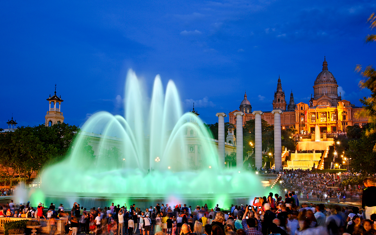 Magic fountain show at Montjuic hill, Barcelona, with crowds watching illuminated water display.