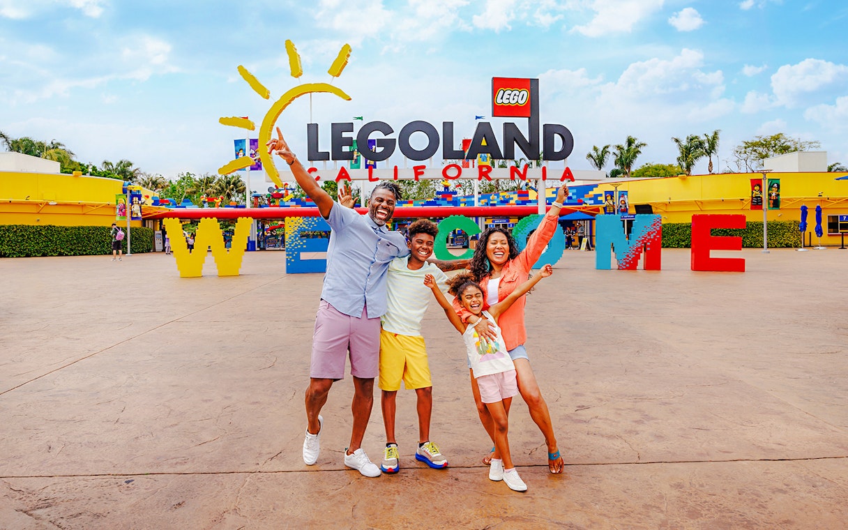 Family posing at the entrance of LEGOLAND California with welcome sign.