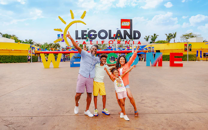 Family posing at the entrance of LEGOLAND California with welcome sign.
