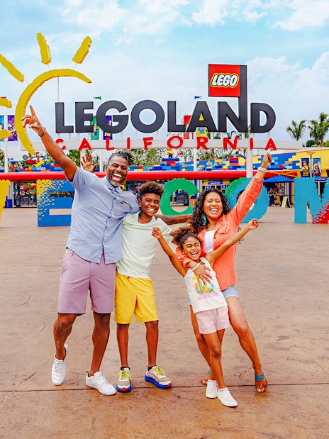 Family posing at the entrance of LEGOLAND California with welcome sign.