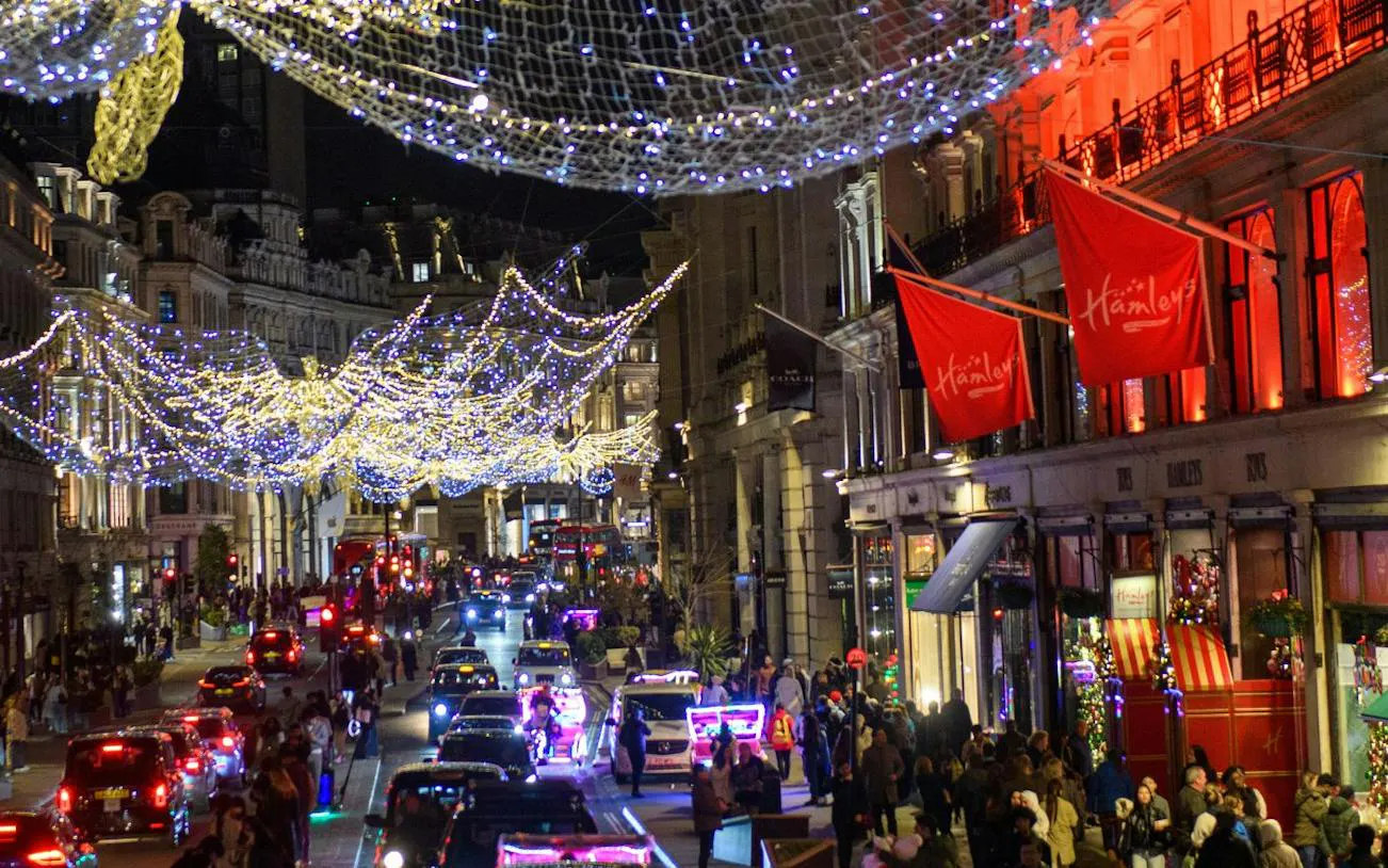 London street with festive Christmas lights and vintage bus tour passing Hamleys store.