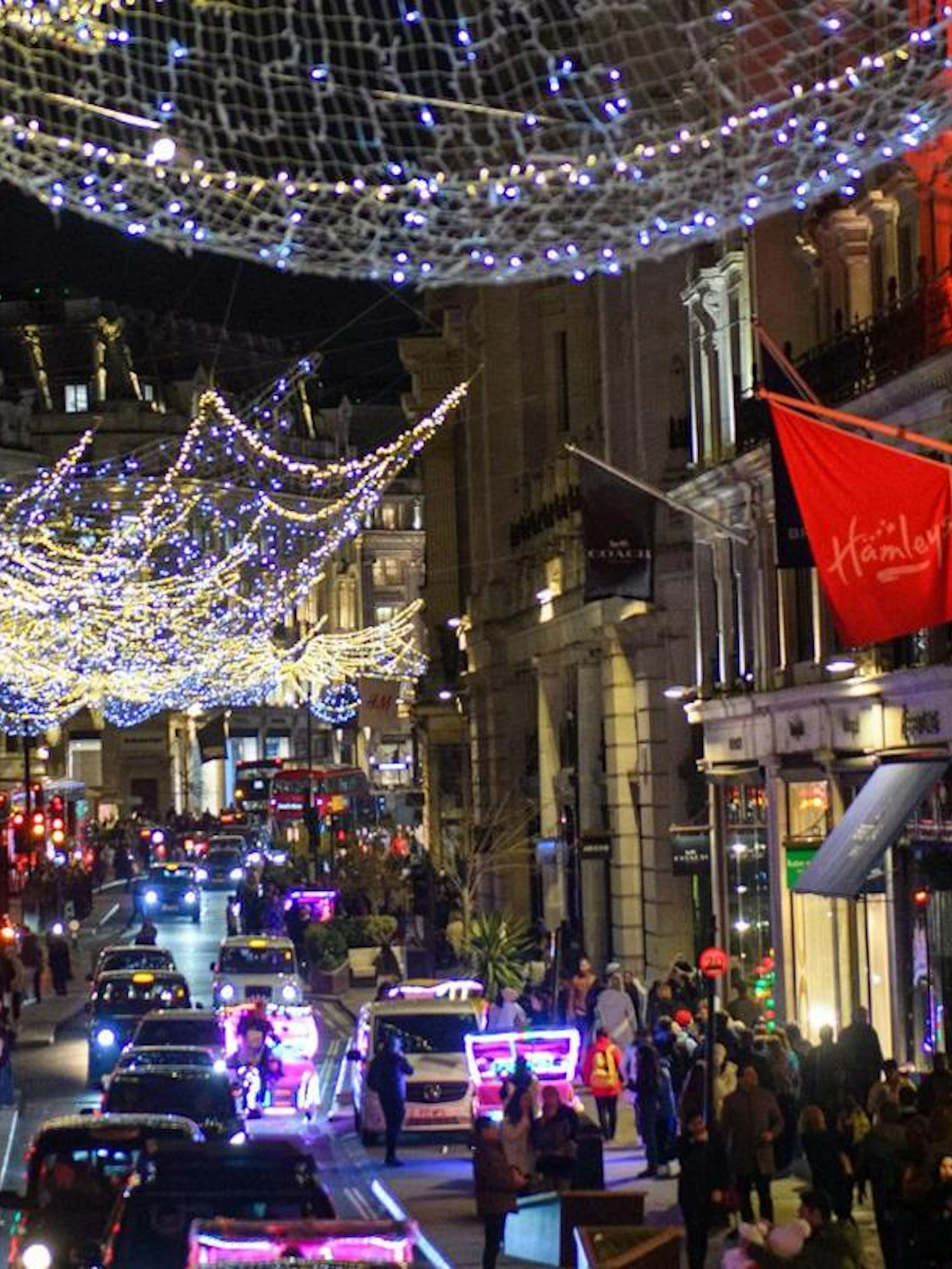 London street with festive Christmas lights and vintage bus tour passing Hamleys store.