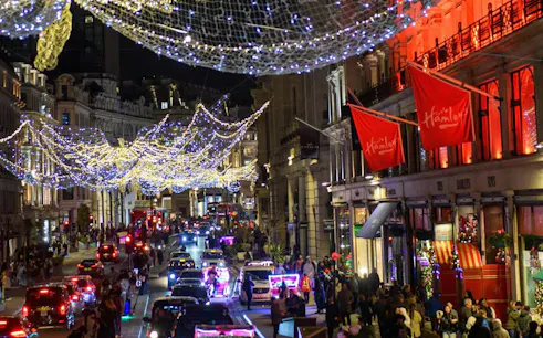 London street with festive Christmas lights and vintage bus tour passing Hamleys store.