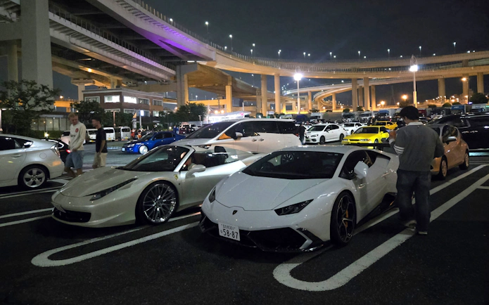 Tokyo car meet at Daikoku PA featuring sports cars under highway lights.