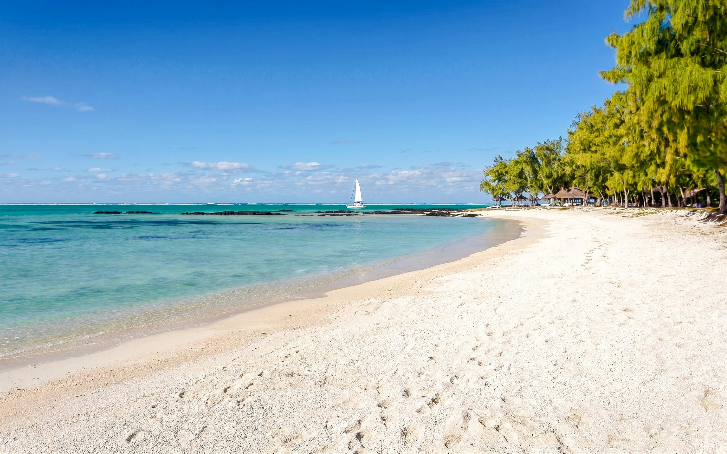 Sandy beach with turquoise water and sailboat at Ile Aux Cerf, Mauritius.