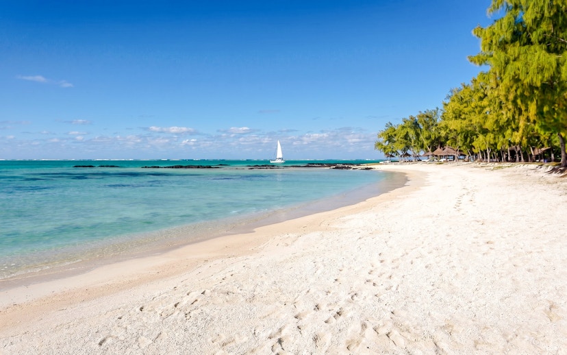 Sandy beach with turquoise water and sailboat at Ile Aux Cerf, Mauritius.