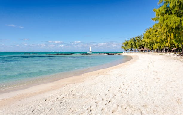 Sandy beach with turquoise water and sailboat at Ile Aux Cerf, Mauritius.
