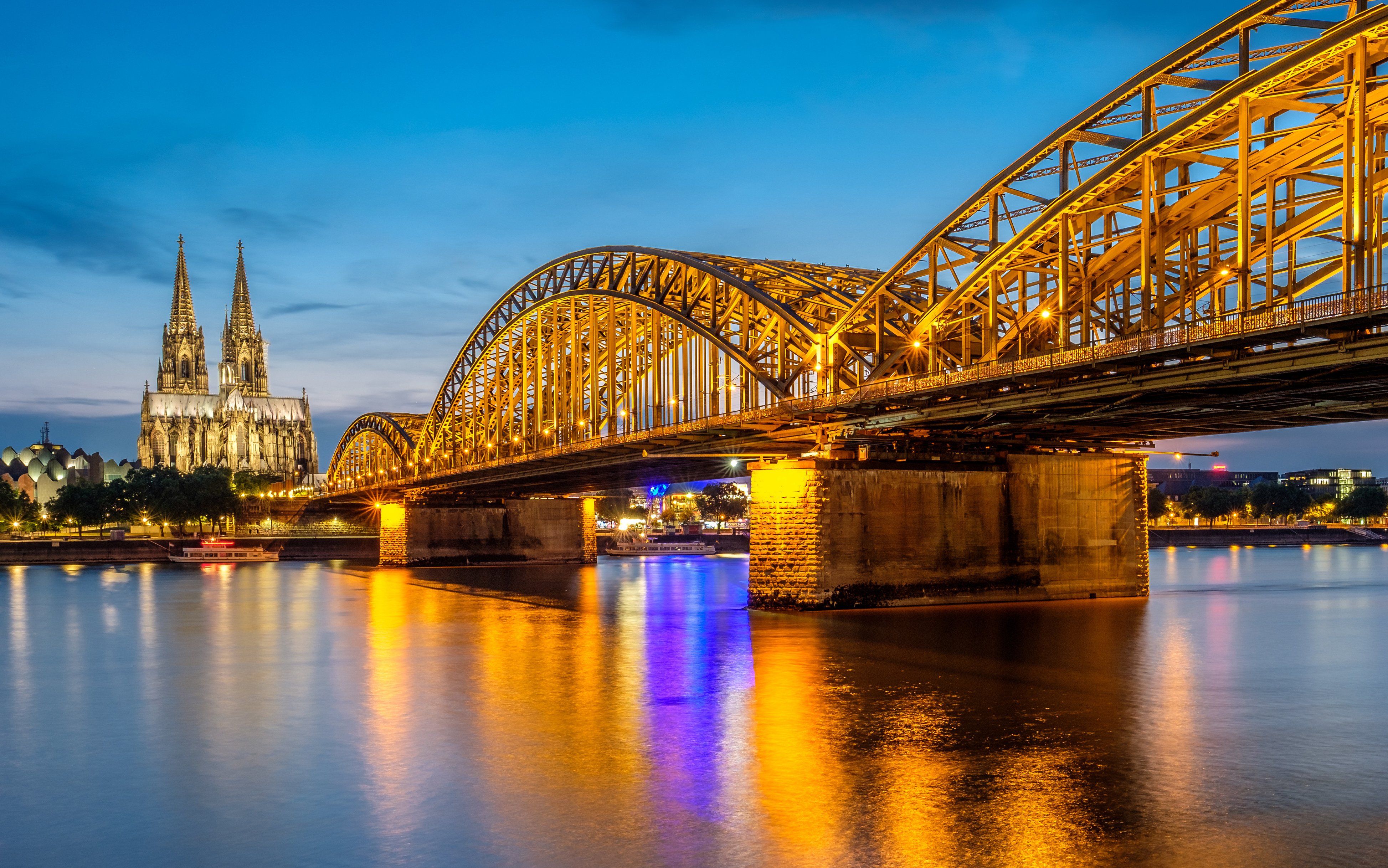 Hohenzollern Bridge illuminated at night with Cologne Cathedral in the background.