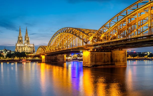 Hohenzollern Bridge illuminated at night with Cologne Cathedral in the background.
