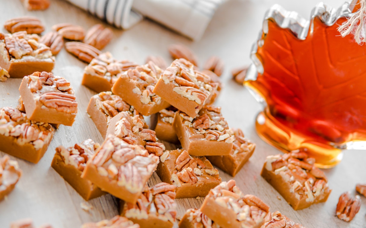 Maple fudge squares topped with pecans next to a maple syrup bottle.