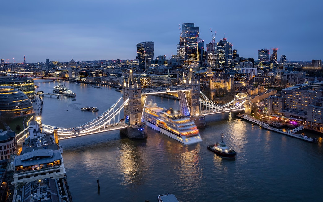 Thames River cruise passing under Tower Bridge in London at dusk.