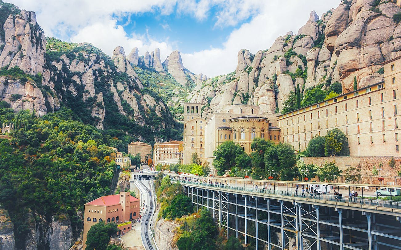 Montserrat Monastery nestled in rocky mountains, with visitors on a walkway, Catalonia, Spain.
