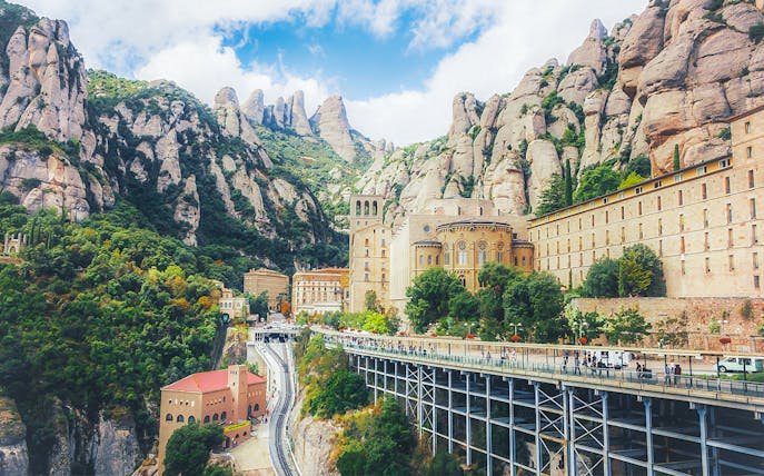 Montserrat Monastery nestled in rocky mountains, with visitors on a walkway, Catalonia, Spain.