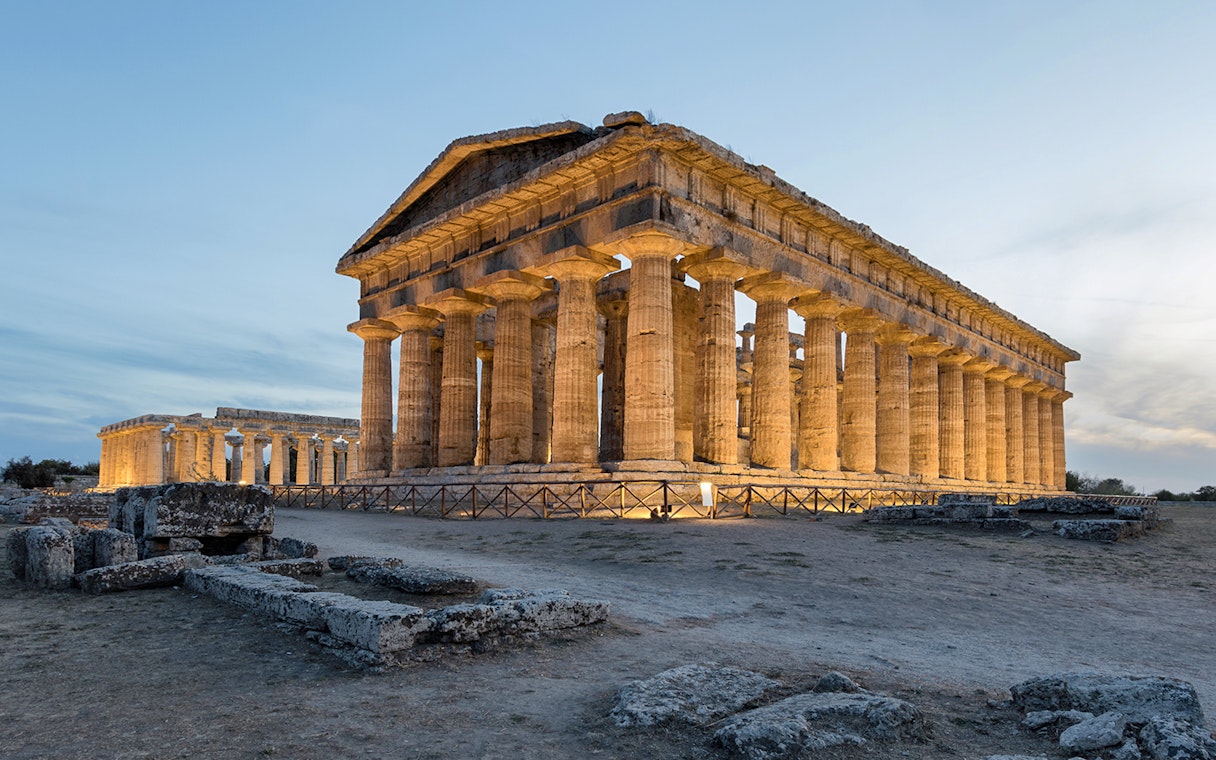 Temple of Poseidon at Paestum Archaeological Park illuminated at dusk.