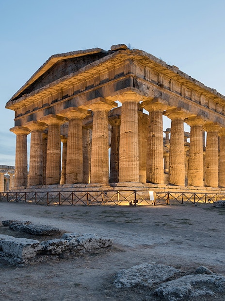 Temple of Poseidon at Paestum Archaeological Park illuminated at dusk.