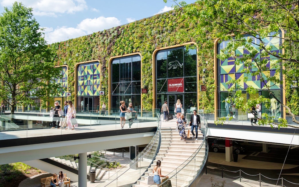Shoppers walking at McArthurGlen Designer Outlet with green wall and colorful patterns.