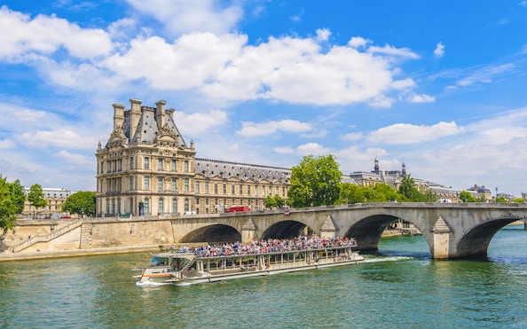 Seine River cruise boat passing by the Louvre Museum in Paris.