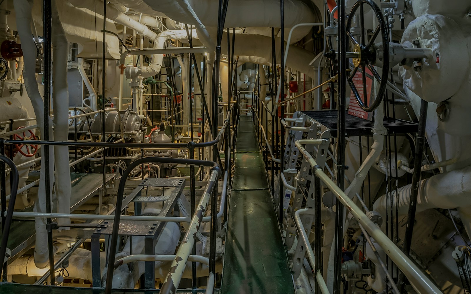 Historic ship's machine room with pipes, valves, and walkways.