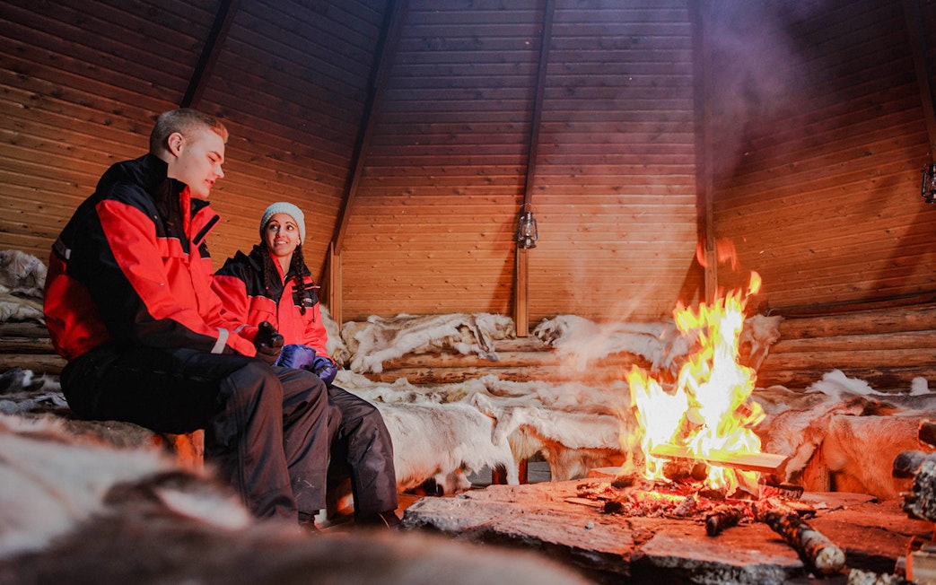 Couple sitting by a fire inside a Finnish kota in Rovaniemi.