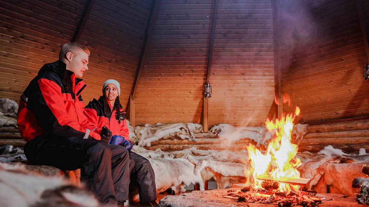 Couple sitting by a fire inside a Finnish kota in Rovaniemi.