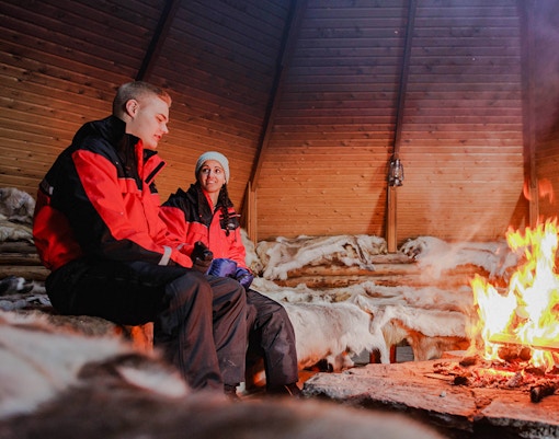 Couple sitting by a fire inside a Finnish kota in Rovaniemi.