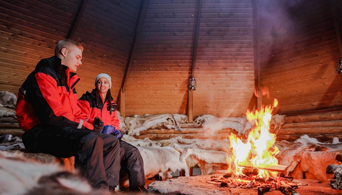 Couple sitting by a fire inside a Finnish kota in Rovaniemi.