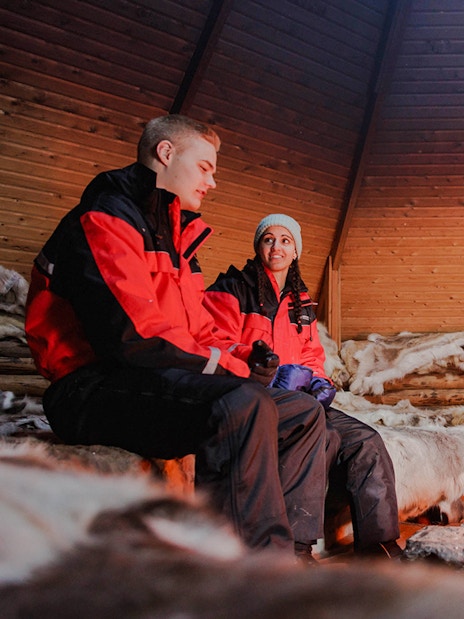 Couple sitting by a fire inside a Finnish kota in Rovaniemi.