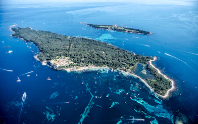 Aerial view of an island with lush greenery and surrounding blue waters seen from Nice sightseeing cruise.