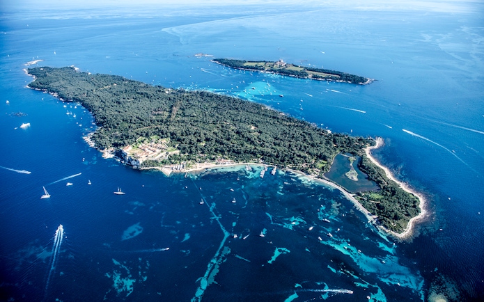 Aerial view of an island with lush greenery and surrounding blue waters seen from Nice sightseeing cruise.