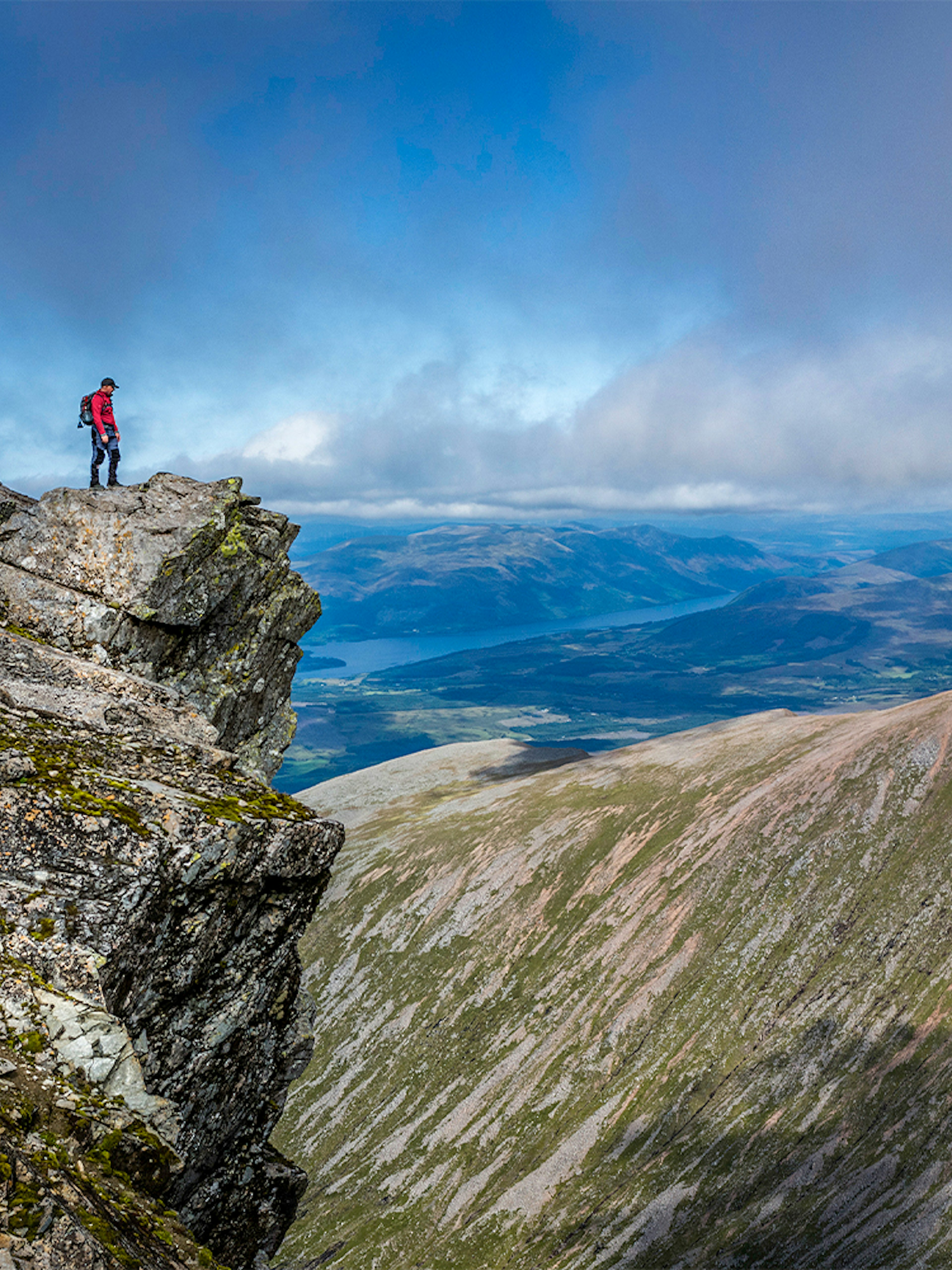 Hiker standing on rocky peak of Ben Nevis with expansive mountain views.