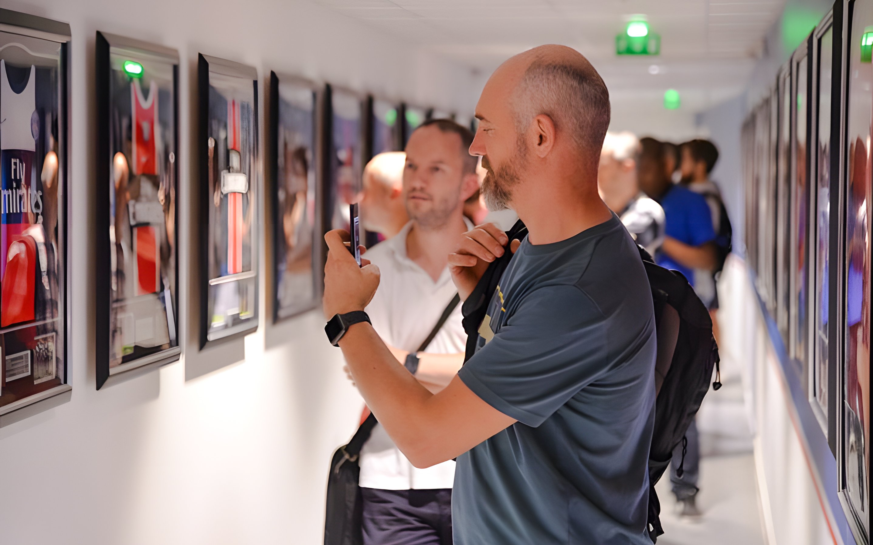 Visitors viewing framed PSG memorabilia in a hallway at PSG Stadium, Paris, France.