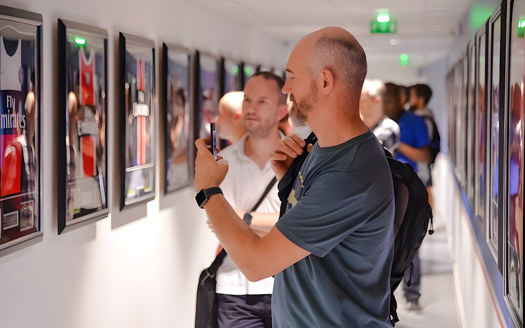 Visitors viewing framed PSG memorabilia in a hallway at PSG Stadium, Paris, France.