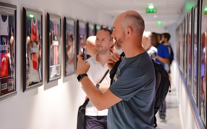 Visitors viewing framed PSG memorabilia in a hallway at PSG Stadium, Paris, France.