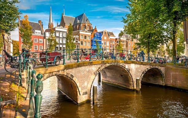 Amsterdam canal bridge with bicycles and historic buildings in the background.