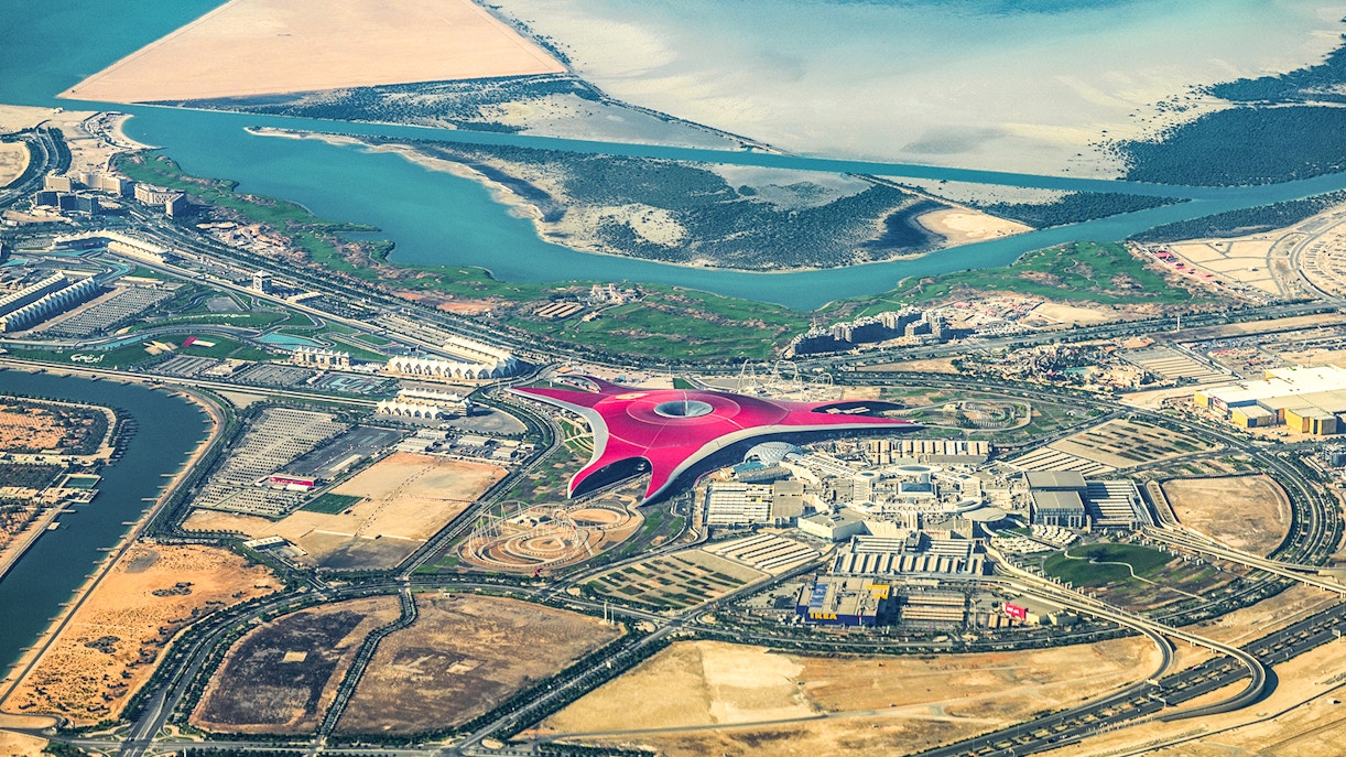 Aerial view of Ferrari World on Yas Island, Abu Dhabi, surrounded by water and desert landscape.