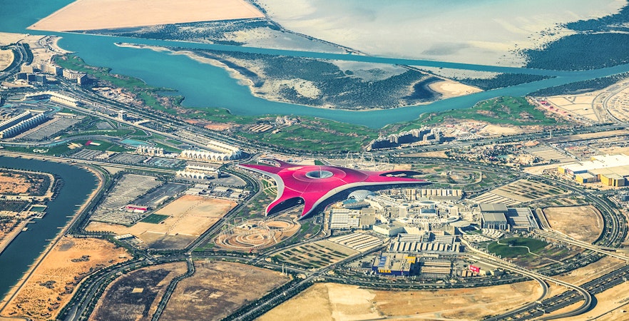 Aerial view of Ferrari World on Yas Island, Abu Dhabi, surrounded by water and desert landscape.