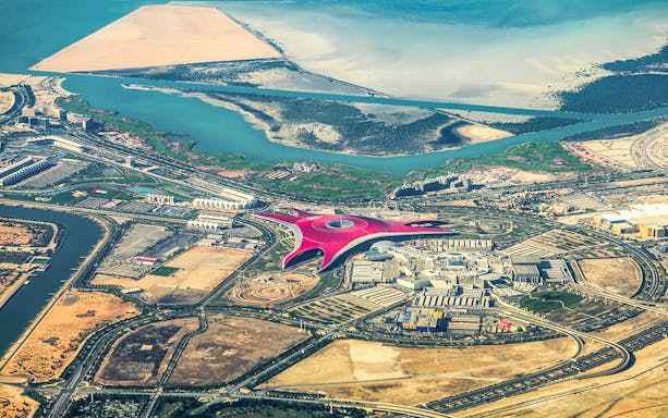 Aerial view of Ferrari World on Yas Island, Abu Dhabi, surrounded by water and desert landscape.