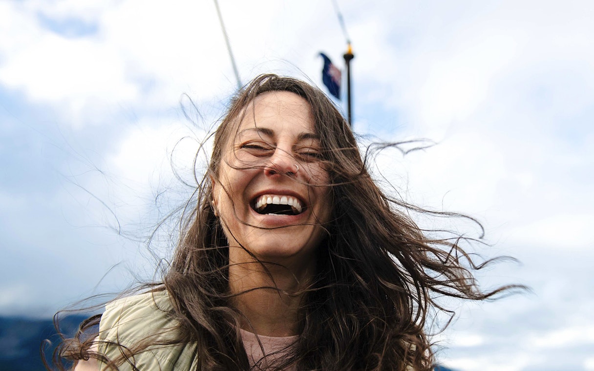 Woman smiling on a boat deck with windblown hair, Queenstown.