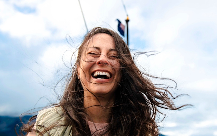 Woman smiling on a boat deck with windblown hair, Queenstown.