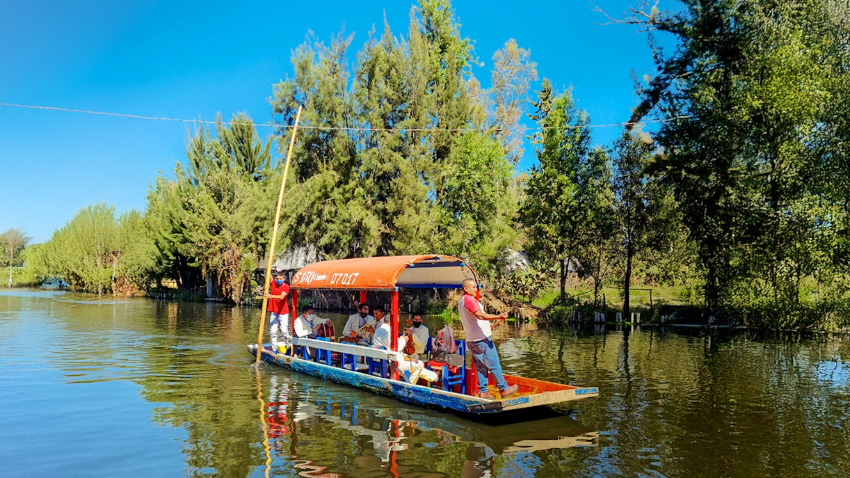 Trajinera boat with people enjoying a festive ride on Xochimilco River, Mexico City.